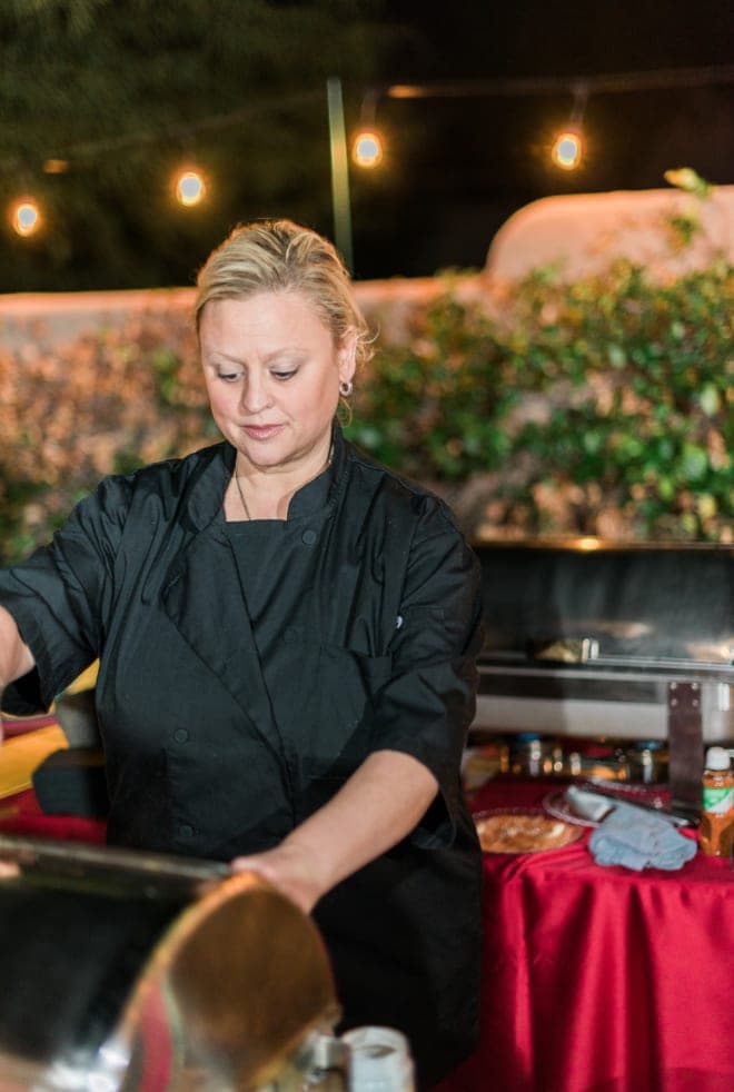 A chef in uniform working a buffet station under string lights at an outdoor event