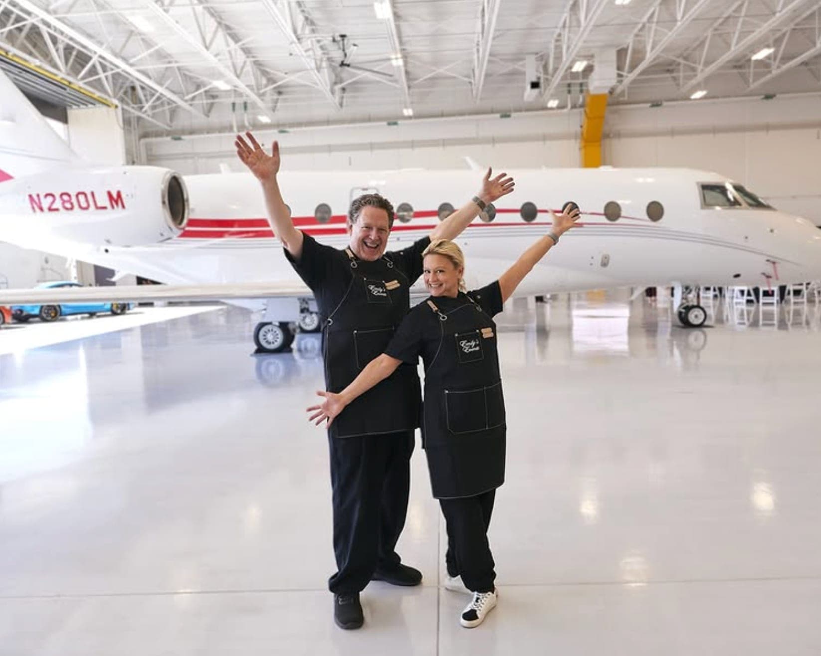 Emily and Rick in Emily's Events aprons celebrating in front of a private jet in a hangar