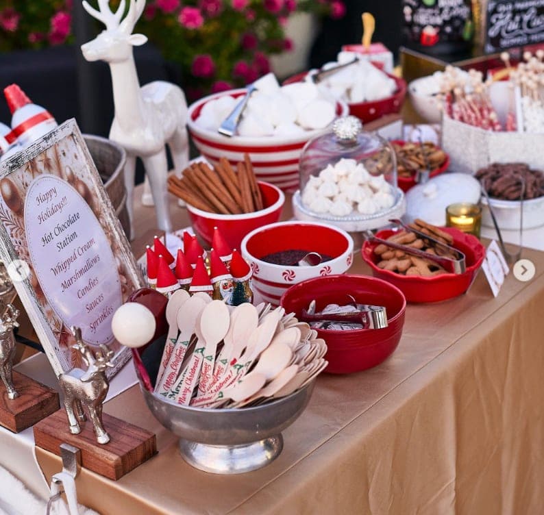A holiday hot-chocolate station with marshmallows, cinnamon sticks, toppings, and candy-cane spoons