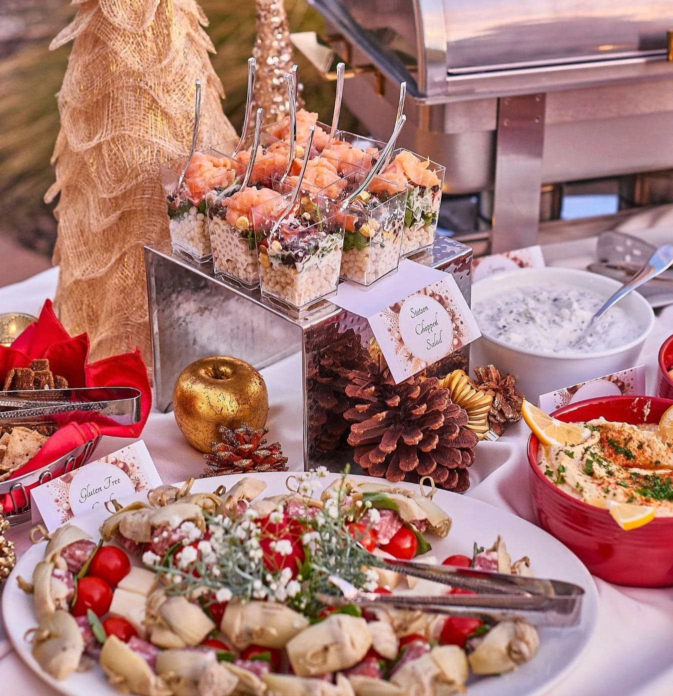 A holiday appetizer spread with shrimp, charcuterie, hummus, and tortellini skewers amid seasonal decor