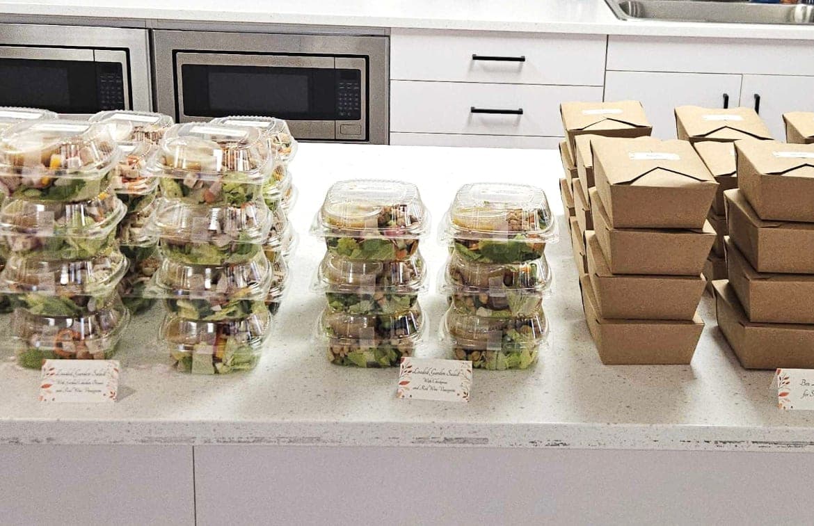 Individually boxed salads and meals on an office kitchen counter, ready for drop-off