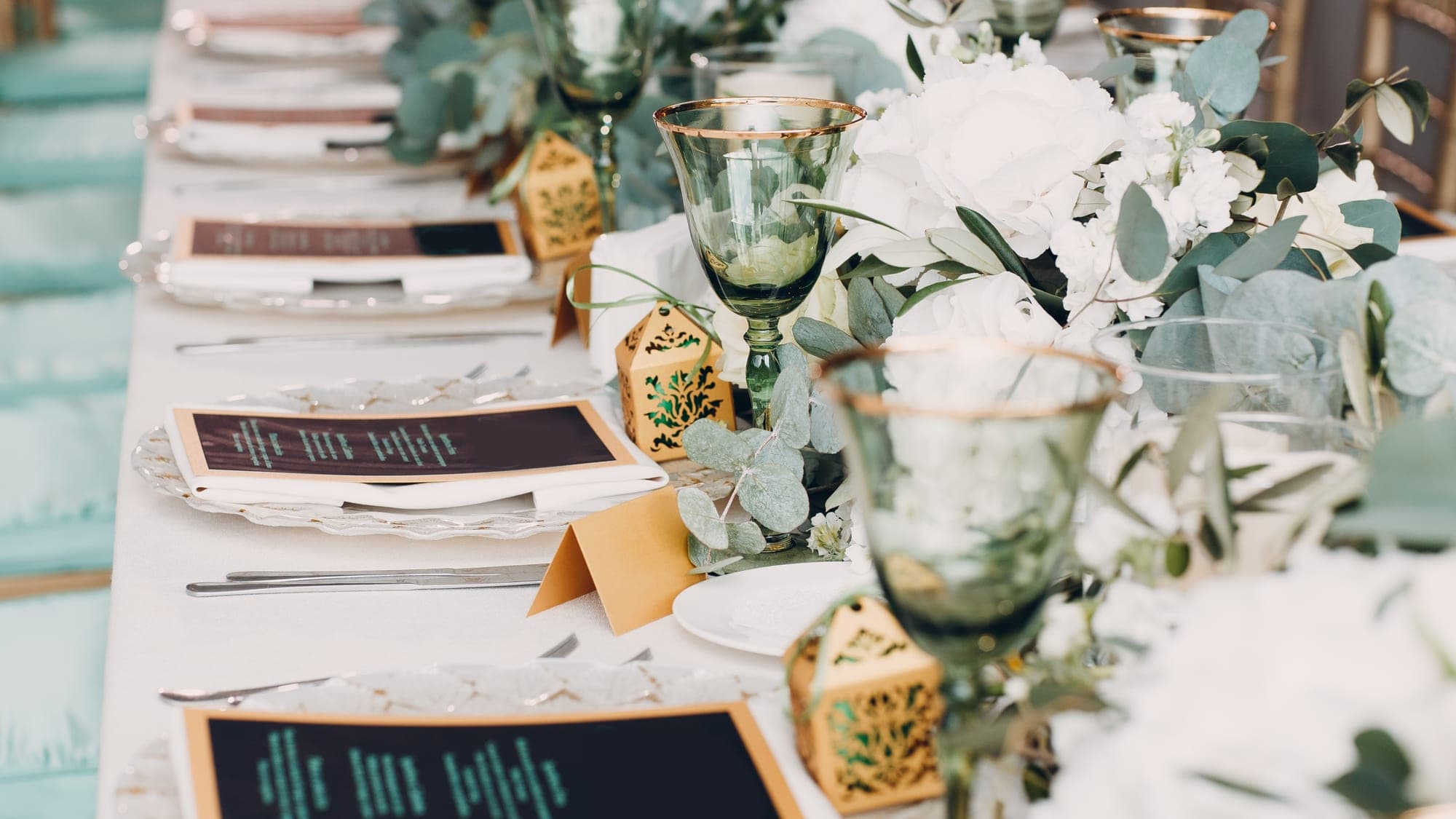 An elegant wedding tablescape with white hydrangeas, eucalyptus, gold favors, and green goblets